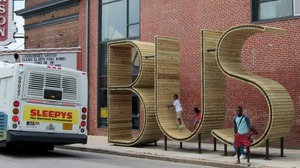 「BUS」というバス停で「BUS」に座ってバスを待つ